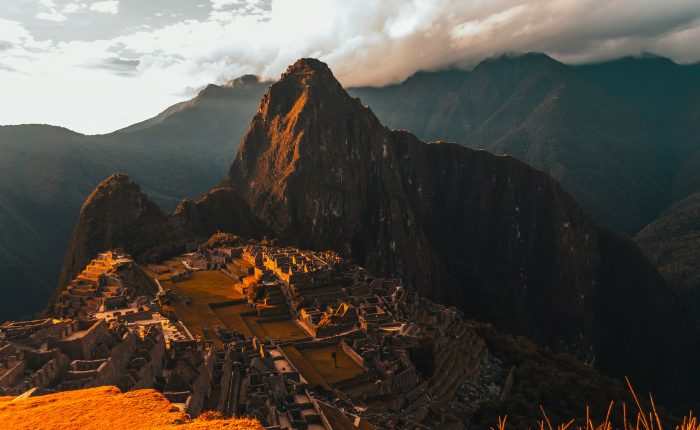 Stone ruins of Machu Picchu illuminated by the warm glow of sunset, with Huayna Picchu mountain in the background.