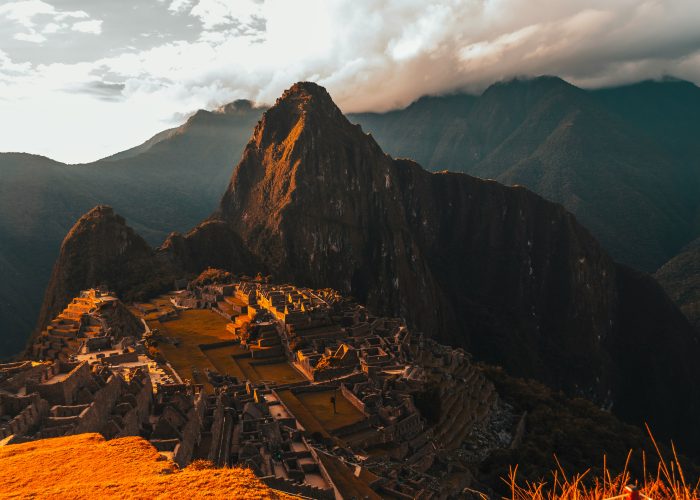 Stone ruins of Machu Picchu illuminated by the warm glow of sunset, with Huayna Picchu mountain in the background.