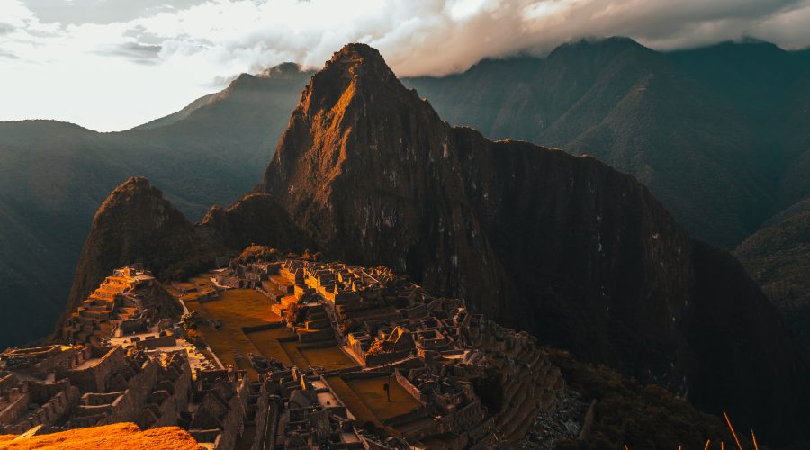 Stone ruins of Machu Picchu illuminated by the warm glow of sunset, with Huayna Picchu mountain in the background.