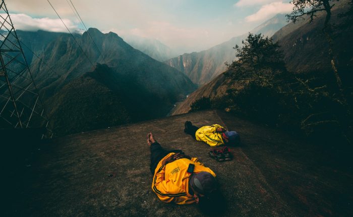 Two hikers in yellow jackets resting on a mountain overlooking a valley in the Peruvian Andes.