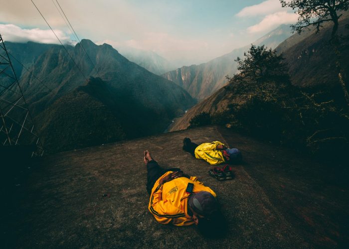 Two hikers in yellow jackets resting on a mountain overlooking a valley in the Peruvian Andes.