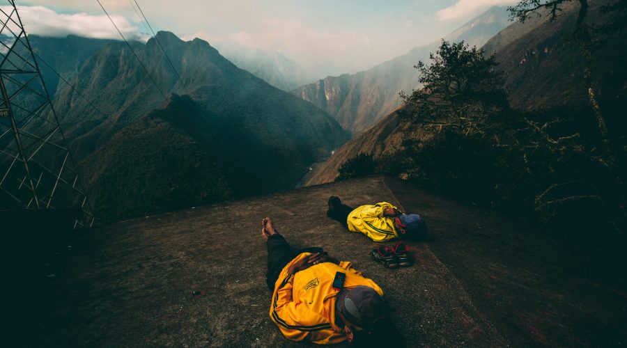 Two hikers in yellow jackets resting on a mountain overlooking a valley in the Peruvian Andes.