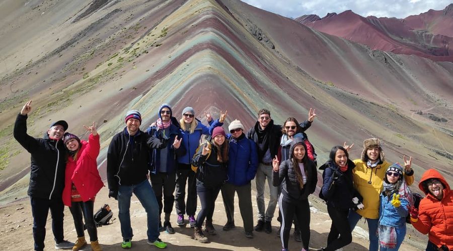 A group of hikers on a Rainbow Mountain Vip guided tour poses at the summit of Rainbow Mountain, Peru, showcasing the stunning landscape.